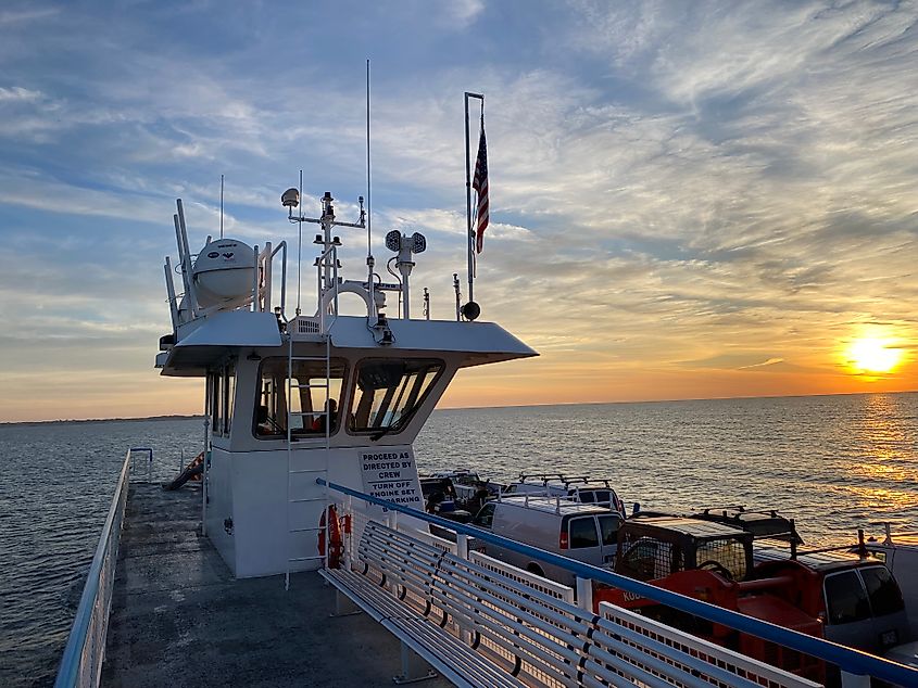 A ferry full of cars heads toward a distant island as the sun rises on the right. 