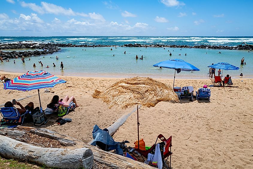 Beachgoers relaxing under colorful umbrellas at Lydgate Beach Park on Kauai, Hawaii.