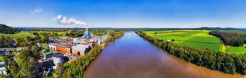 Broadwater sugar mill on banks of Richmond river across sugarcane farmed fields and planes in aerial wide panoramic view. Via Shutterstock / Taras Vyshnya