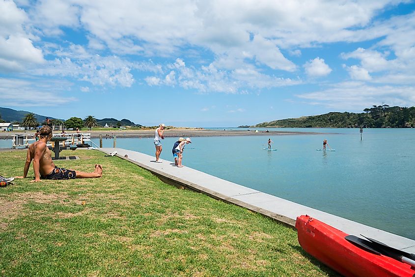 Summer fun in Raglan children fishing with mother on harbour edge while man sits in sun January 14, 2017 Raglan New Zealand