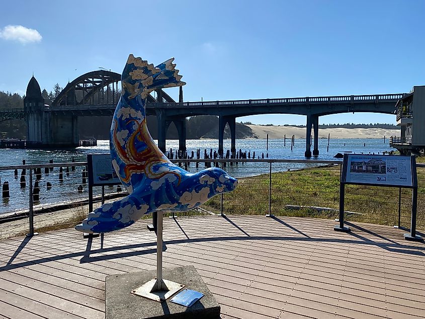 A blue painted sea lion statue stands before an ornate drawbridge with riverside dunes peaking through in the background.