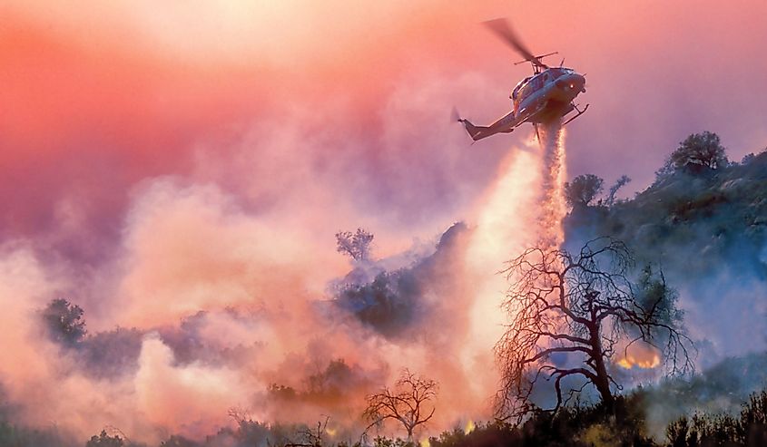 A helicopter dropping water on a California wildfire in rugged terrain