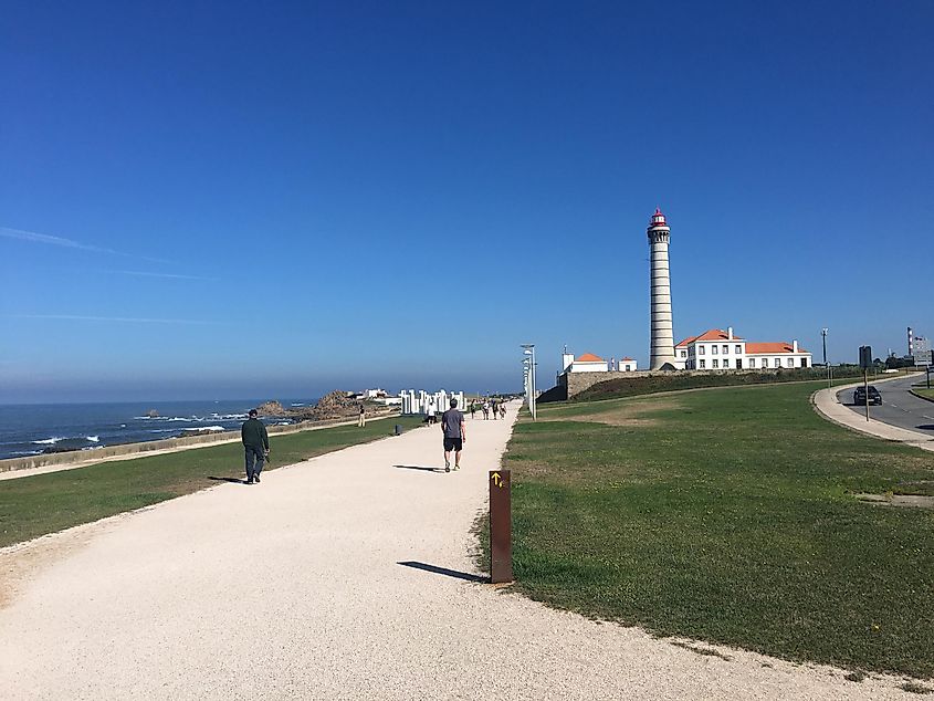 A wide walking path leading towards a oceanside lighthouse in the distance.