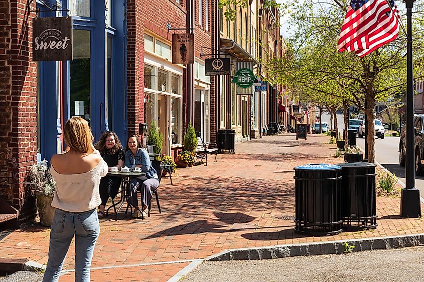 JONESBOROUGH, TN, USA--9 APRIL 2021:Thin, blonde woman with back to camera takes a picture of two friends seated at a sidewalk table, in front of the 'Downtown Sweet' coffee shop.