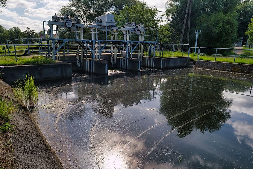 Water treatment facility features mechanical systems managing water flow with algae visible on the surface.