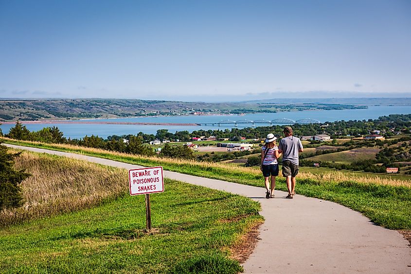 Chamberlain SD - Couple walks on path overlooking Missouri River with a snake warning sign.