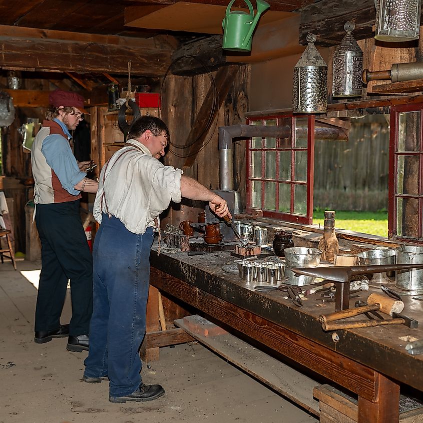 Two costumed historians work alongside each other inside the tin shop at Old Sturbridge Village, Sturbridge, Massachusetts.