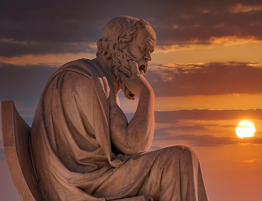 A marble statue of Socrates under a dramatic sky.