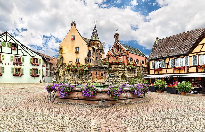 Square with colorful traditional french houses and fountain with statue of Pope Leo IX in Eguisheim, France