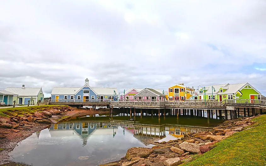 Colorful seaside buildings on a cloudy day are reflected in calm water. Bright hues of blue, yellow, pink, and green create a cheerful, vibrant atmosphere.