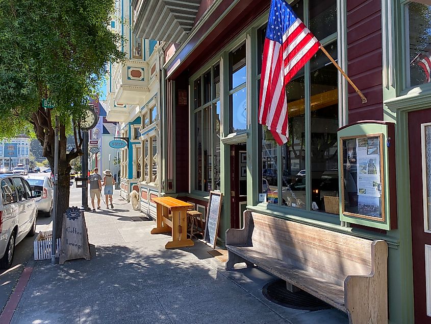 A couple walks past a coffee shop with an American flag on a beautiful sunny day.