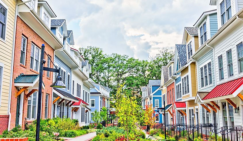 Row of colorful, red, yellow, blue, white, green painted residential townhouses, homes, houses with brick patio gardens in summer