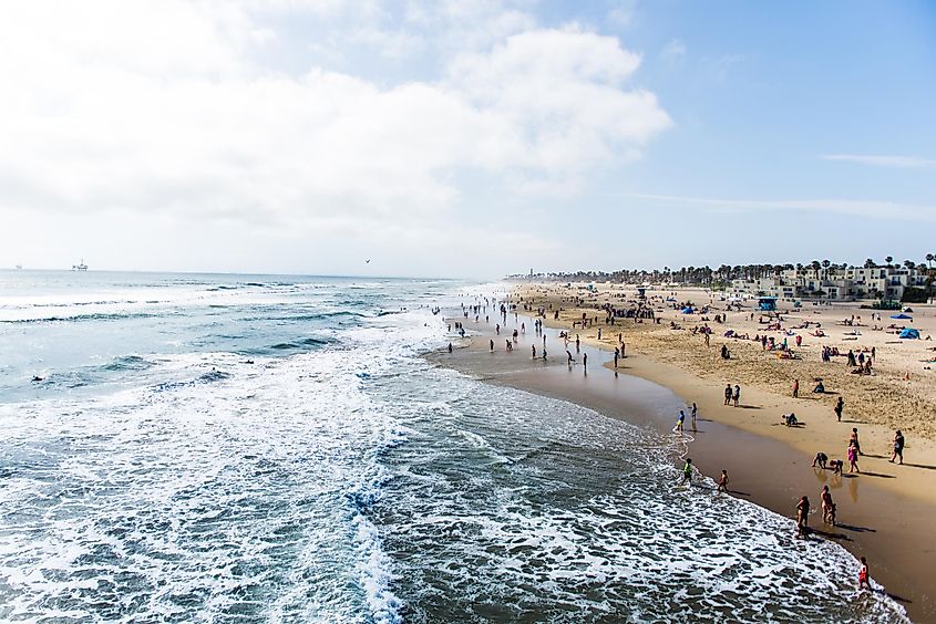 Crowds of tourists and sun bathers having fun and swimming at Huntington Beach, California.