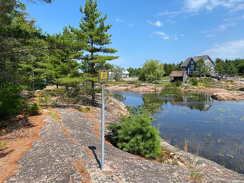A subtle hiking marker stands on the granite trail, leading the way through jack pines and past a private island cabin.
