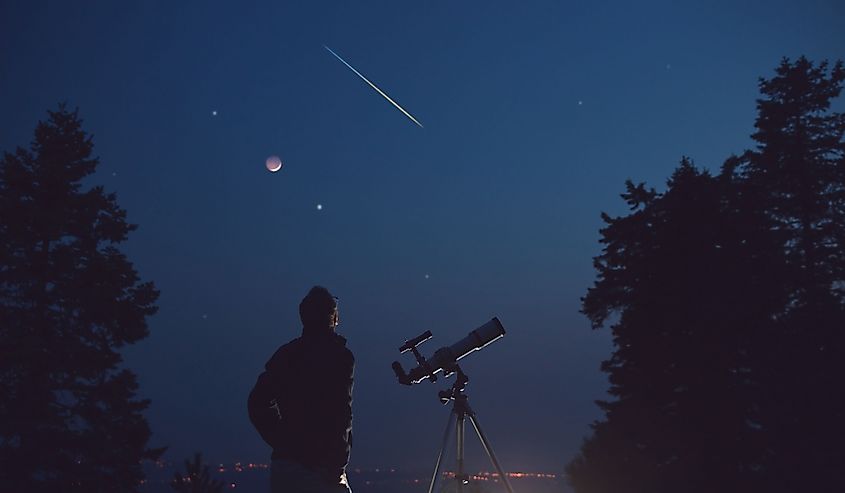 Silhouette of a man, telescope, stars, planets and shooting star under the night sky.