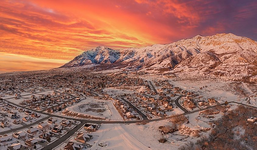 Aerial drone view high above the neighborhoods of North Ogden and Pleasant View Utah with an incredible orange winter sunset and fresh fallen snow.