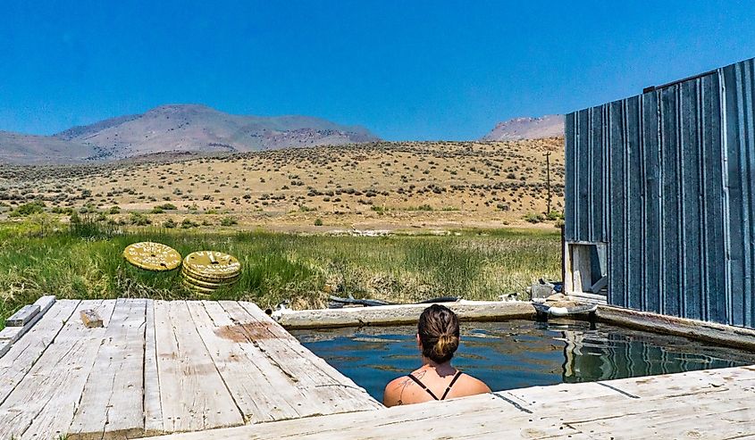 Young woman soaking in the Alvord Desert Hot spring in southeastern Oregon, with view on the Steens mountain