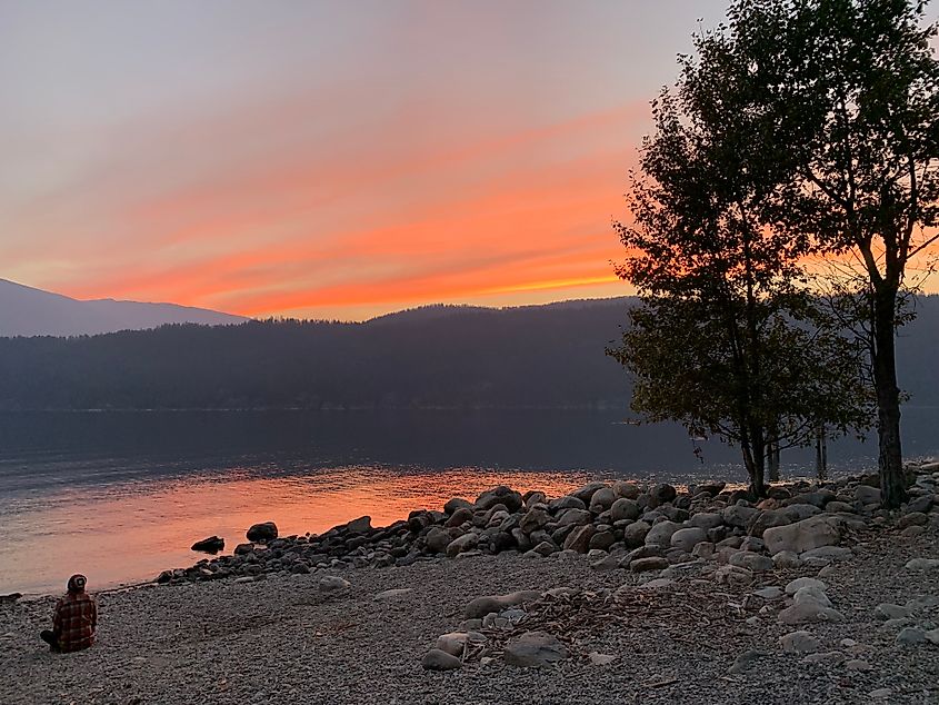 A man in plaid meditates on a rocky shore beneath a pastel mountain skyline sunset.