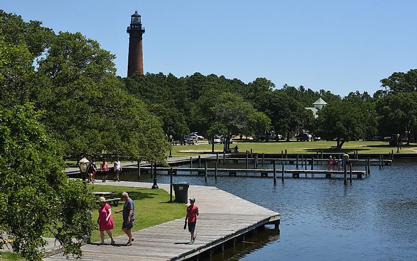People walking along the boardwalk, The Currituck lighthouse looms in the distance at historic Corolla Park.