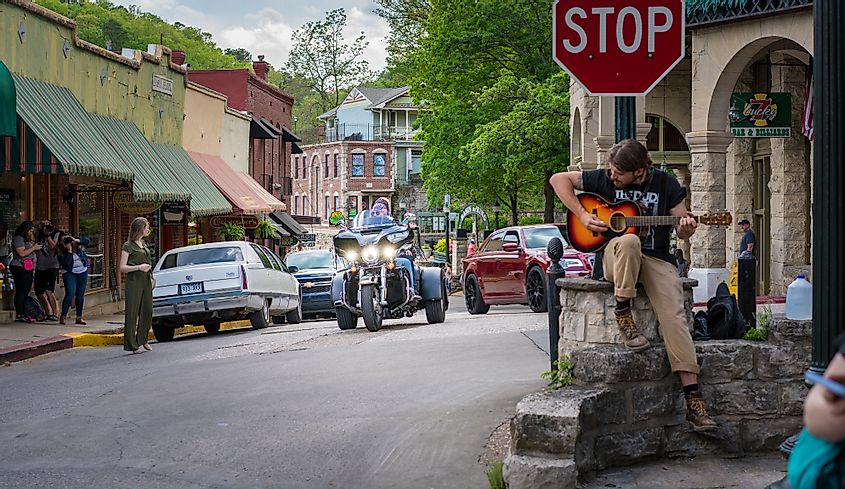 Eureka Springs, Arkansas, Biker visitors riding motorcycle downtown Eureka Springs, Man playing guitar at a stop sign, freedom tourism on two wheels, vintage small American town.