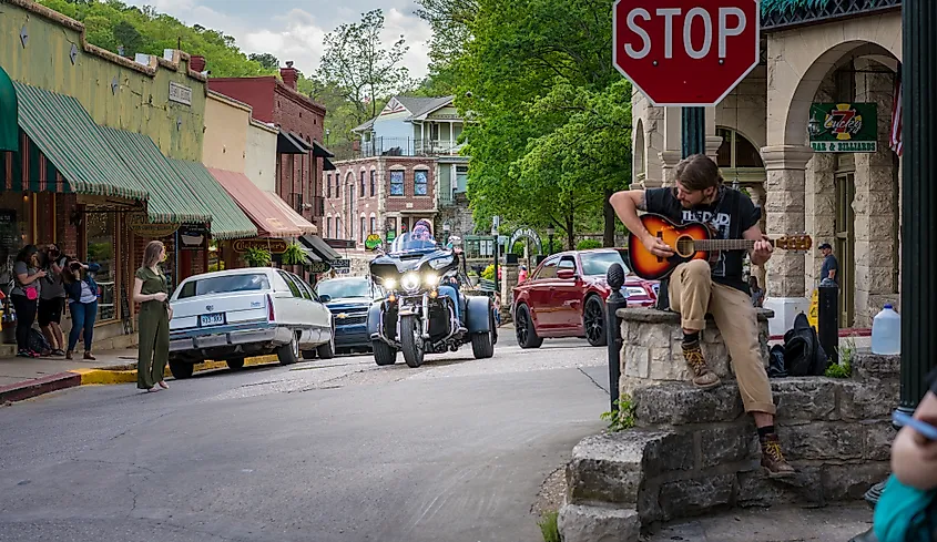 Biker visitors riding motorcycles downtown Eureka Springs, Arkansas, USA. A man playing guitar at a stop sign adds to the ambiance of freedom tourism on two wheels in this vintage small American town.