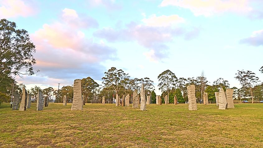 Standing stones arranged in a grassy field with trees in the background.