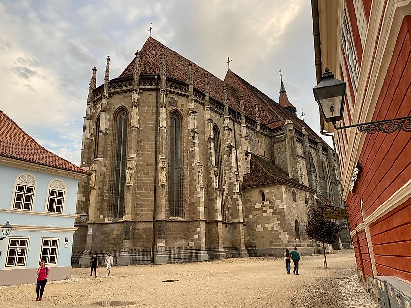 A large gothic cathedral looking extra gothic between two colorful buildings on a cloudy day.