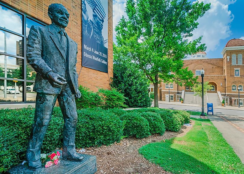 Bronze statue of a civil rights leader outside a brick building with a church visible in the background.