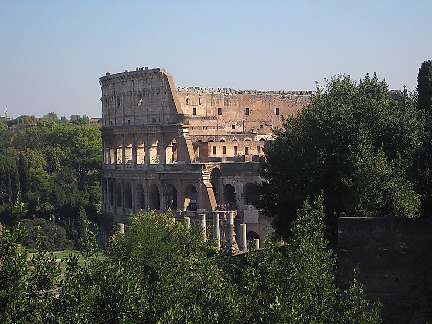View of the Colosseum in Rome from an elevated garden, showing the amphitheater’s arched stone exterior and surrounding trees.