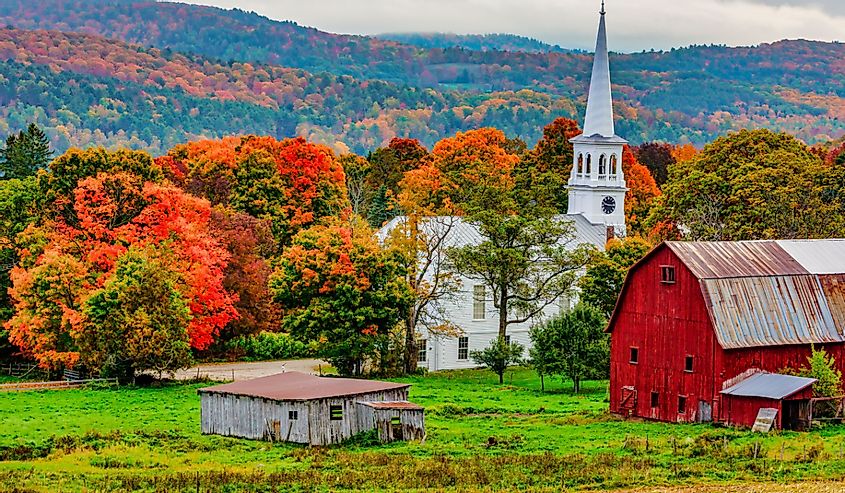 Red barn and church next to a harvested cornfiield with the Autumn colors in the background