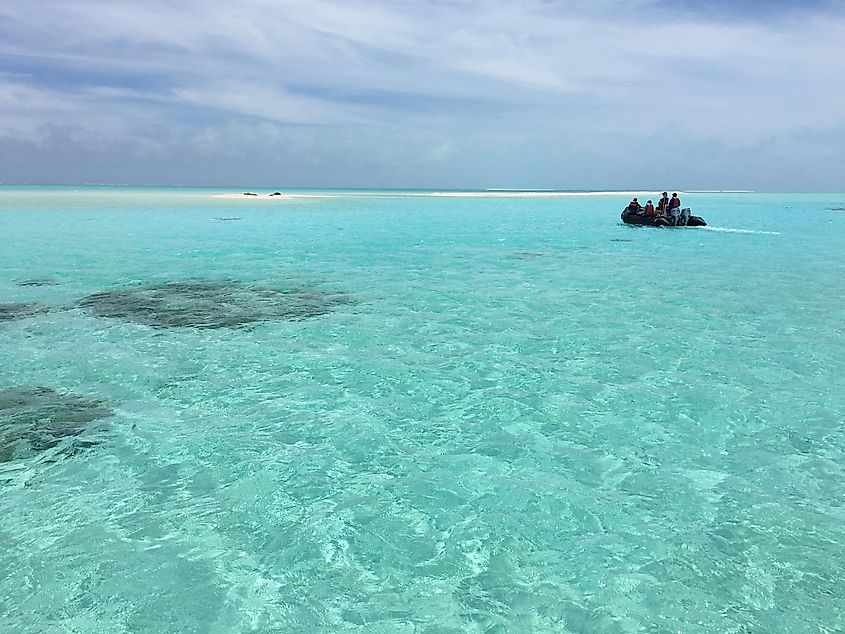 A small boat cruises through a turquoise lagoon towards a sand spit with endangered Hawaiian monk seals on it at Pearl and Hermes Reef, Papahanaumokuakea Marine National Monument, Hawaii.