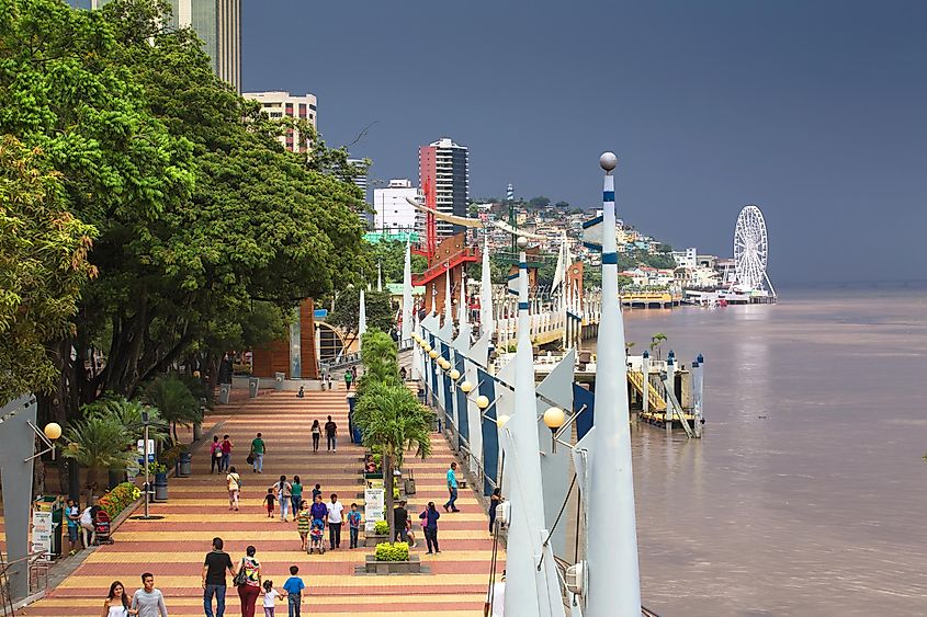 A riverside walkway. A ferris wheel is in the background and storm clouds are rolling in