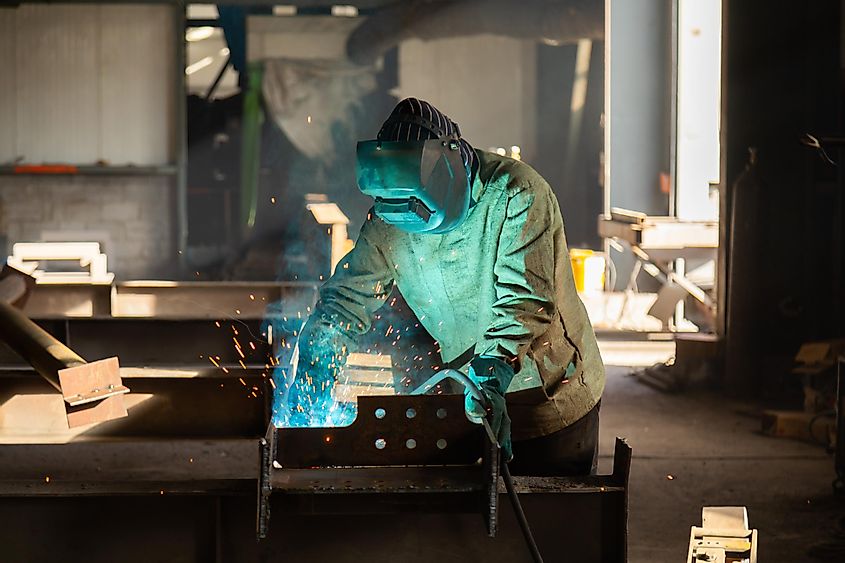 Industrial welder with a torch and protective helmet in big hall welding metal profiles