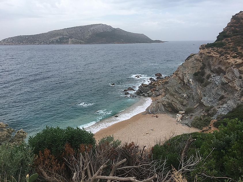 A hidden beach beckons one down from the steep cliffs. One sunbather can be seen as the waves roll in. 