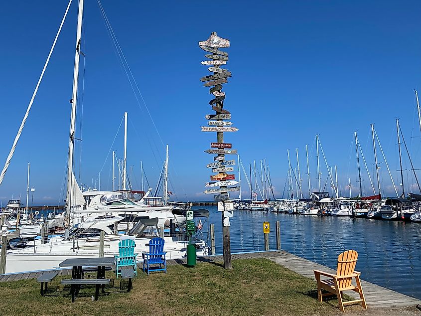 A marina with a tower of wooden signs citing the distance to each respective town.