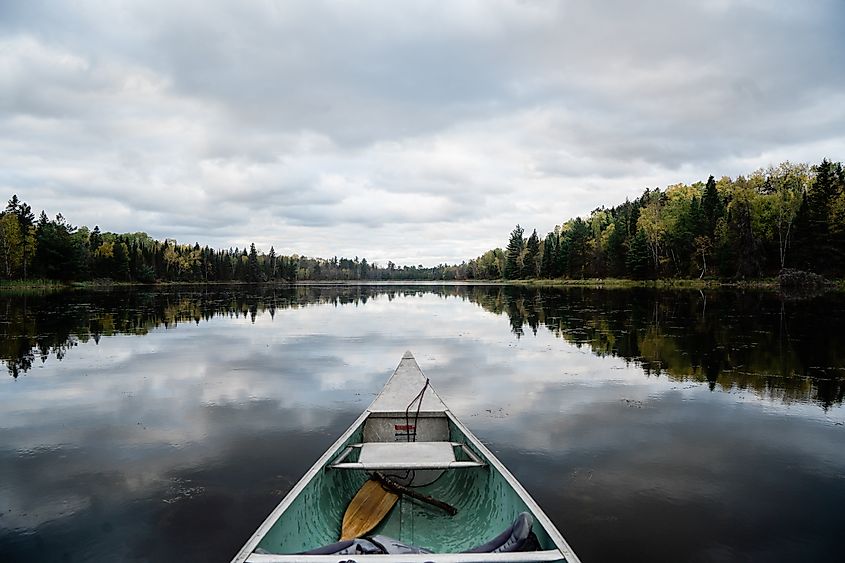 Canoe gliding over flat, calm water in Voyageurs National Park, surrounded by forested shoreline and open sky