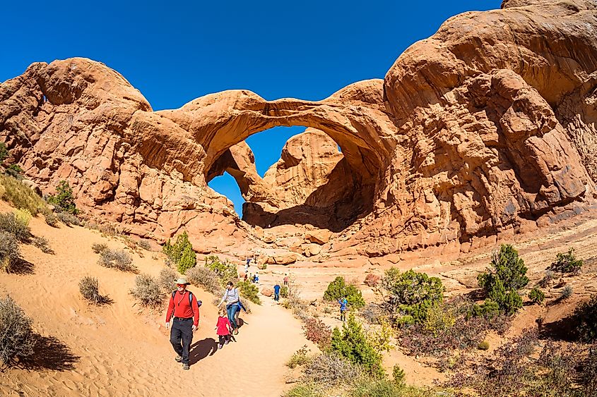 Tourists enjoying the natural beauty of the Double Arch in Arches National Park in Moab, Utah. Editorial credit: Fotoluminate LLC / Shutterstock.com