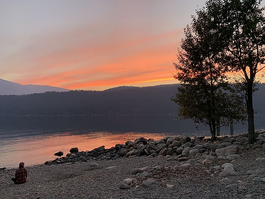 A man sits in meditation on a rocky beach during an orange-pink post-sunset glow