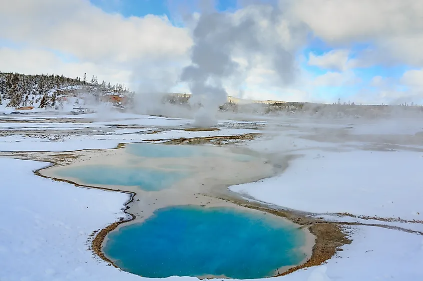 Geysers emitting steam in the snow-covered landscape of Yellowstone National Park in winter.
