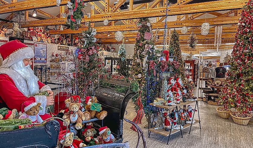 Festive store interior with Christmas trees, a Santa figure in a sleigh with teddy bears, and holiday decorations. Warm, cheerful atmosphere.