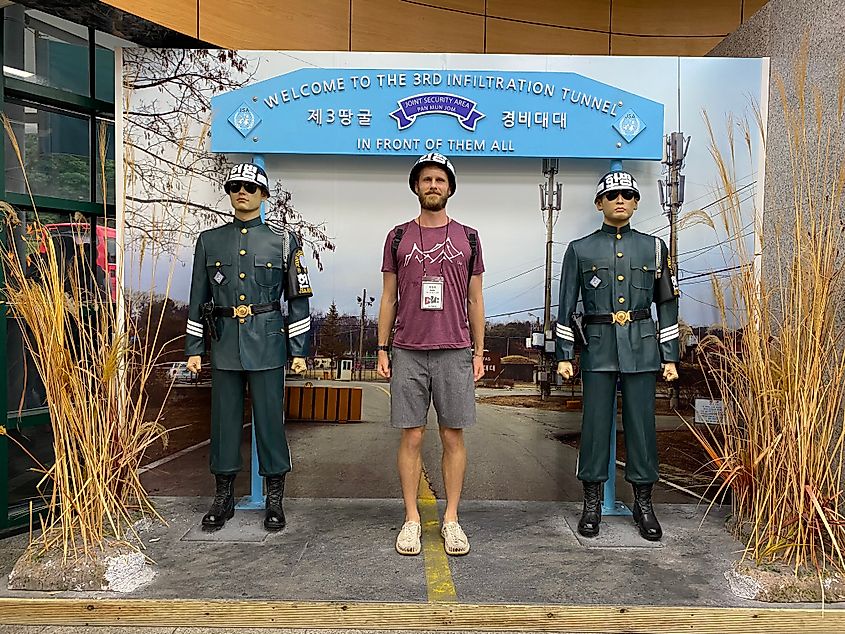 A male tourist poses with a helmet beside two Korean soldier statues