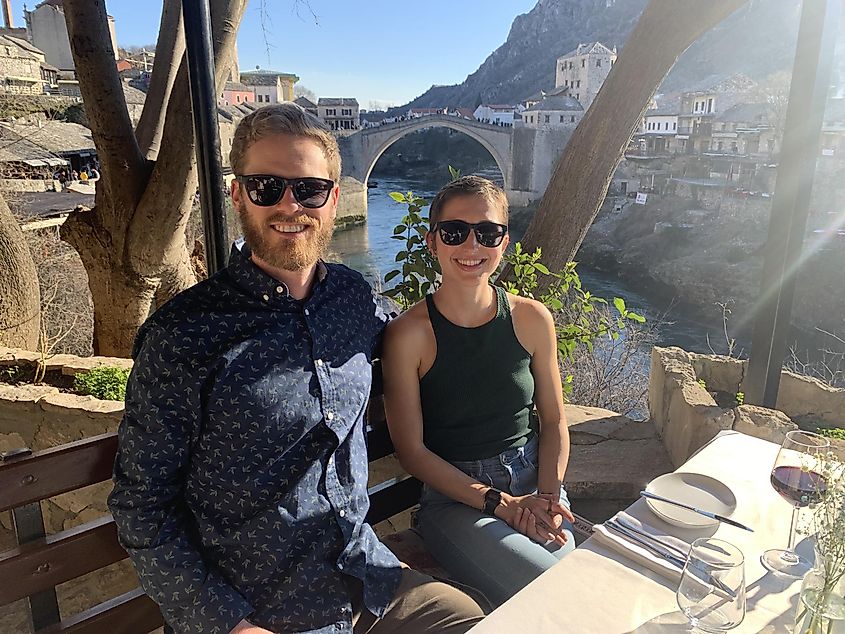 A couple poses for a picture at a riverside restaurant overlooking the iconic Old Bridge of Mostar. 