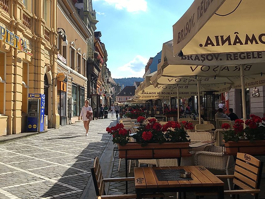 A woman walks a brick-lined tourist street, filled with tables and umbrellas. 
