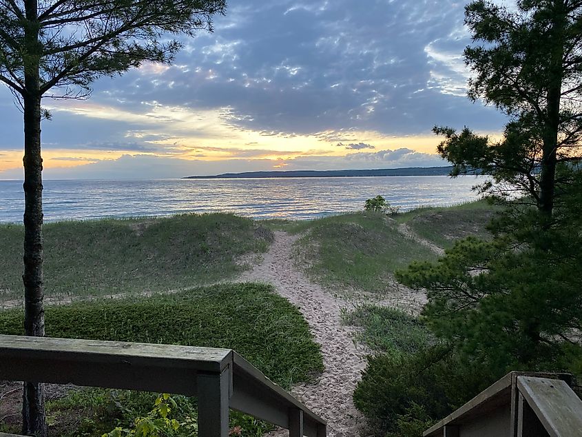 A cloudy sunset seen from a wooden platform above a grassy beach.