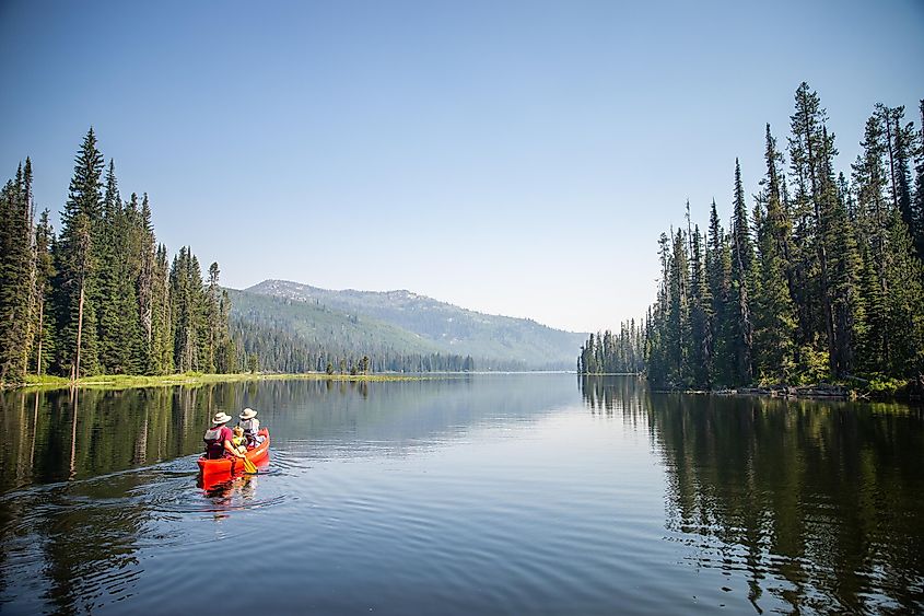 Kayakers glide smoothly across the clear, tranquil waters of Upper Payette Lake, surrounded by the picturesque Idaho landscape.