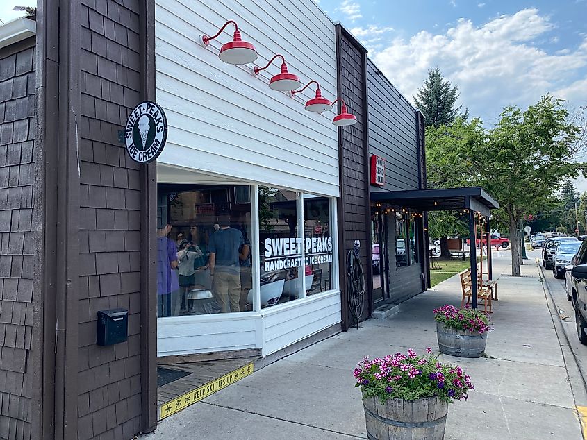 Flowerpots and trees line the sidewalk outside of a popular ice cream shop.