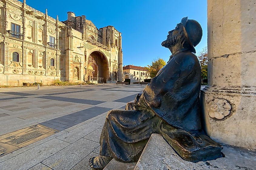 A statue of a Christian pilgrim, sits outside of a stately building in a public square in Spain.