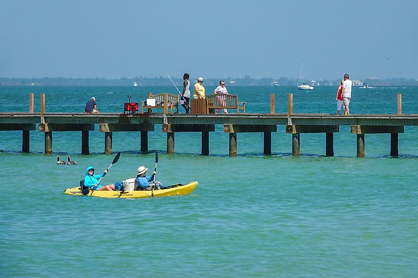 Two kayakers paddle near a public pier that attracts fishermen and other sightseers in the Anna Maria Island