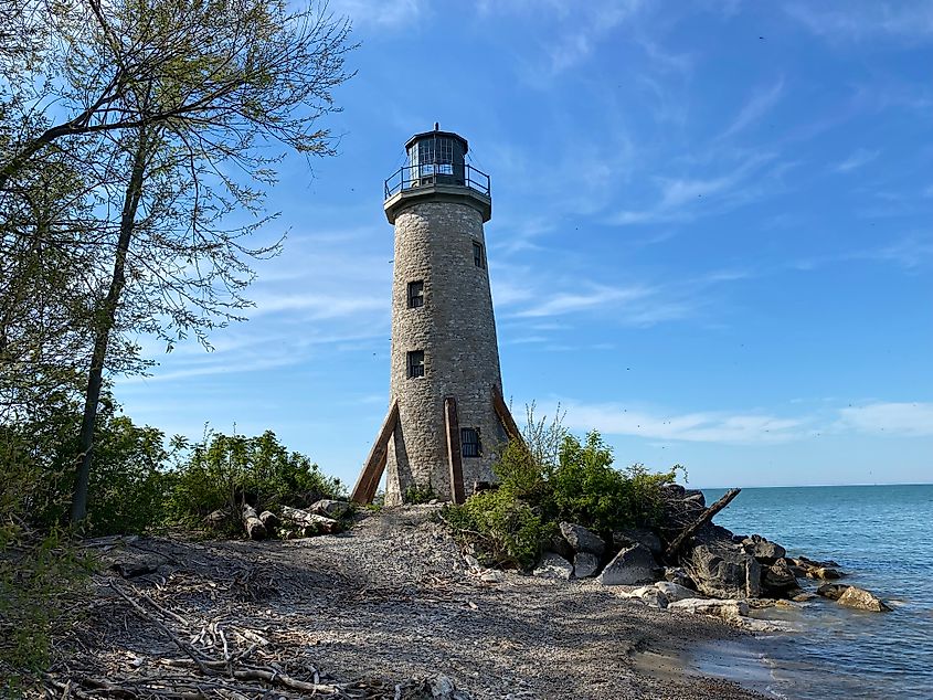 An old stone lighthouse stands atop a narrow and wild lake beach.