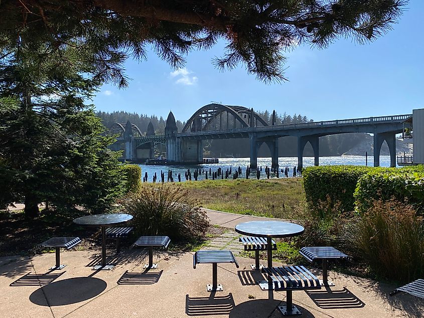 An old steel river bridge as seen from a quaint park with empty picnic tables. 